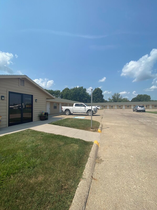 A building with a large garage door, a parking lot, and a grassy area.