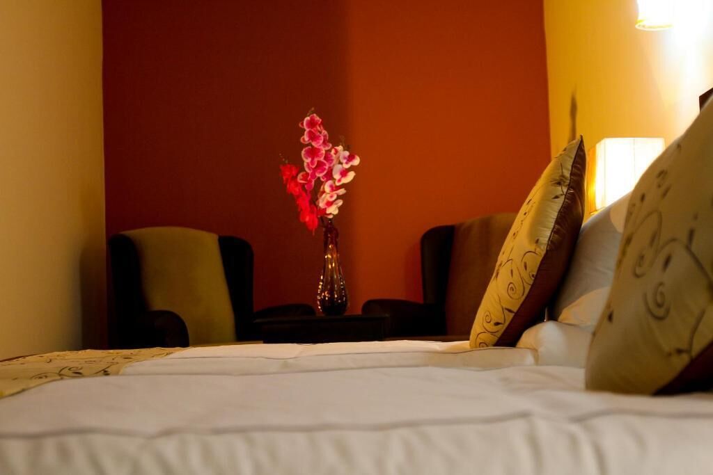 A hotel room with a bed, a vase with flowers, two armchairs, and patterned pillows.
