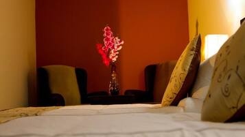 A hotel room with a bed, a vase with flowers, two armchairs, and patterned pillows.