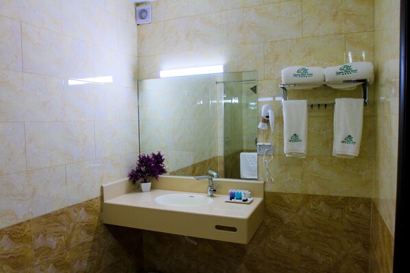 Un baño con lavamanos, espejo, toallero y una planta en maceta.