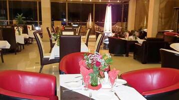 A spacious dining area with multiple tables and chairs, large windows, and a modern interior design.