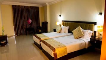 A hotel room with two beds, a large window with curtains, a chair, and a nightstand with a lamp.