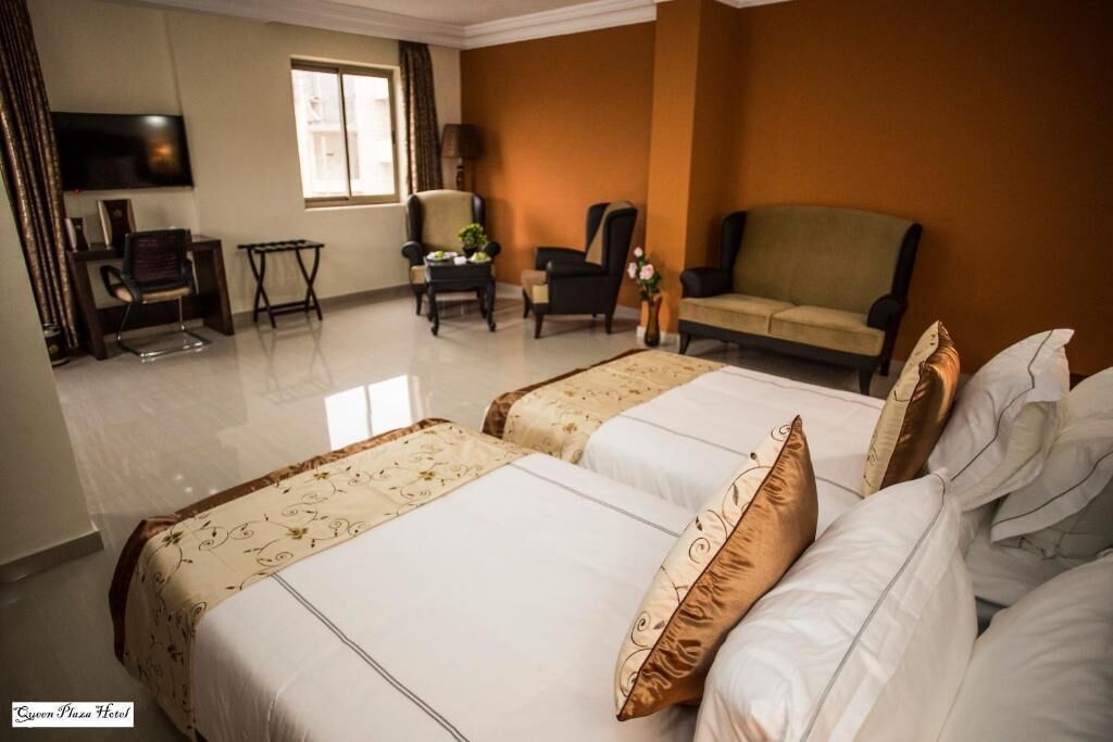 A hotel room with two beds, a sofa, a TV, and a desk with a chair.