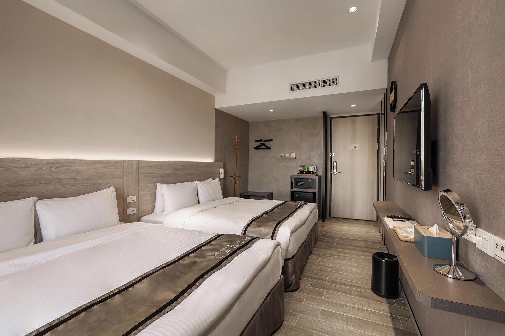 A hotel room with two beds, a desk with a mirror, and a television on the wall.