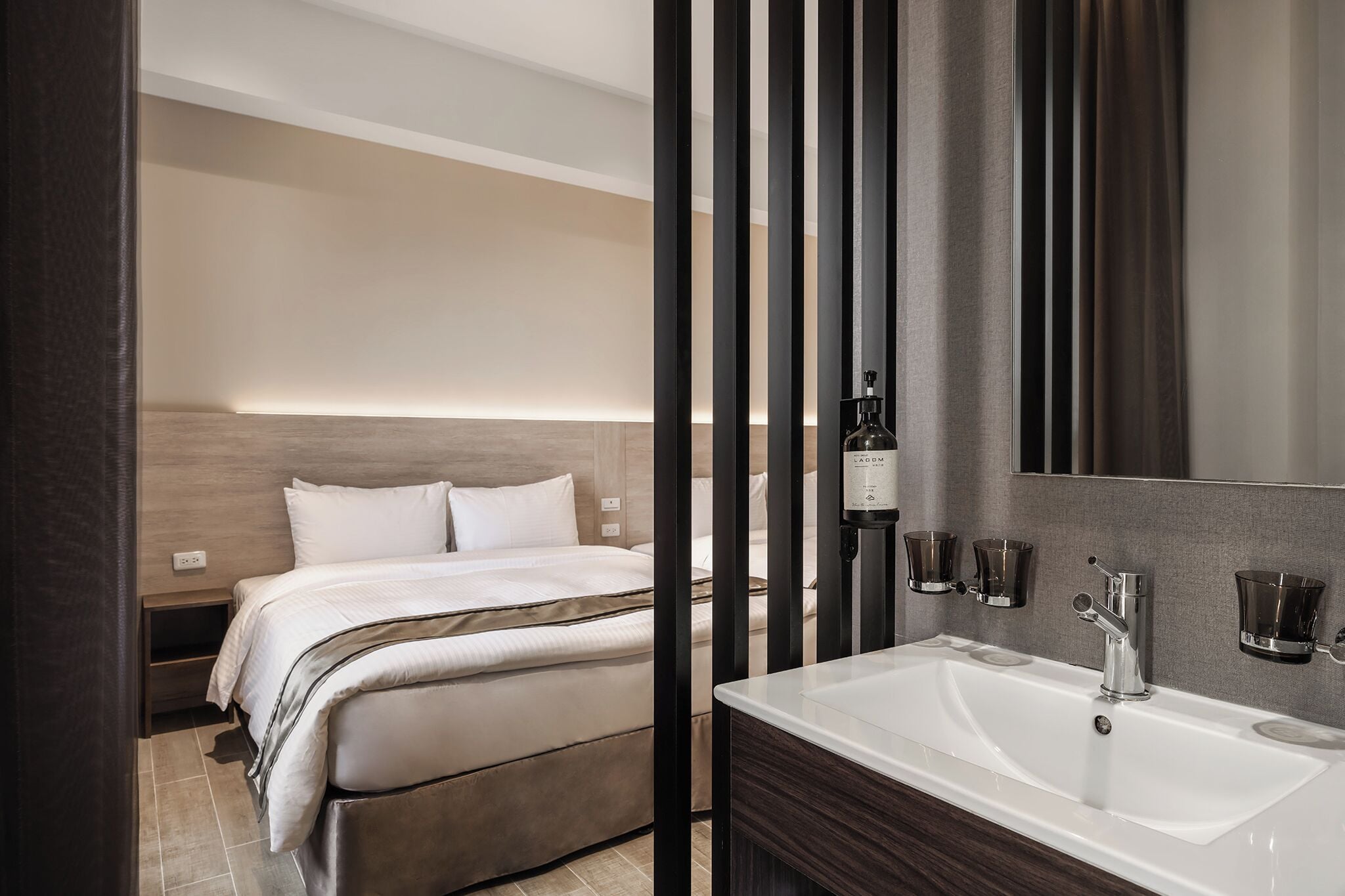 A modern hotel room with a large bed, a white bathroom with a sink and mirror, and a wooden headboard.