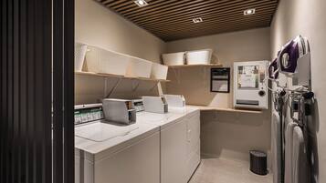 Een moderne wasserette met witte wasmachines, drogers en planken met manden.
