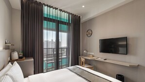 A hotel room with a bed, a desk, a chair, a TV, and a window with curtains.