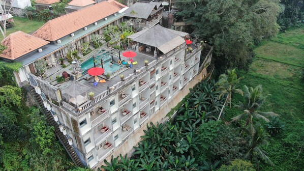 A multi-story hotel with a rooftop pool area, outdoor seating, and lush surrounding vegetation. - Kawi Resort A Spiritual Sanctuary to Escape (Tampaksiring)