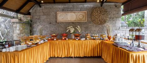 A buffet setup with a variety of food items and decorative elements on a long table, set against a stone wall with a wooden ceiling.