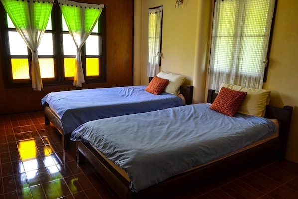 Dos camas individuales con ropa de cama azul, un cabecero de madera y piso de baldosas.