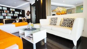 A modern living room with a white sofa, zebra-patterned pillows, and a glass coffee table. - Portrait Pranburi Hotel (Pranburi)