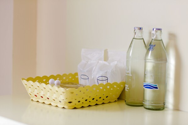 Una cesta amarilla con tapa, una bolsa de papel blanca y dos botellas transparentes con etiquetas azules sobre una mesa.