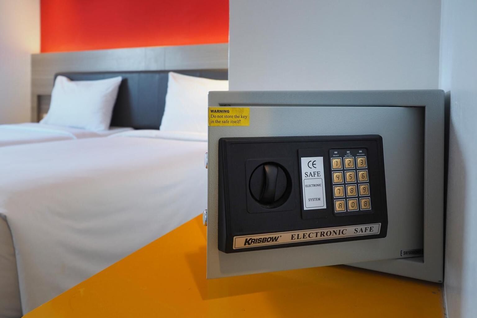 A hotel room with a bed, a wall-mounted electronic safe, and a CE safe label.