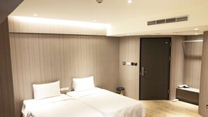 Habitación de hotel con dos camas, suelo de madera, una puerta y una mesita.