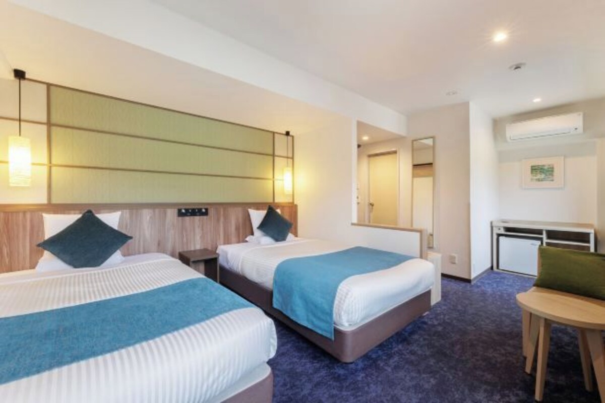 A hotel room with two beds, a desk, and a chair.