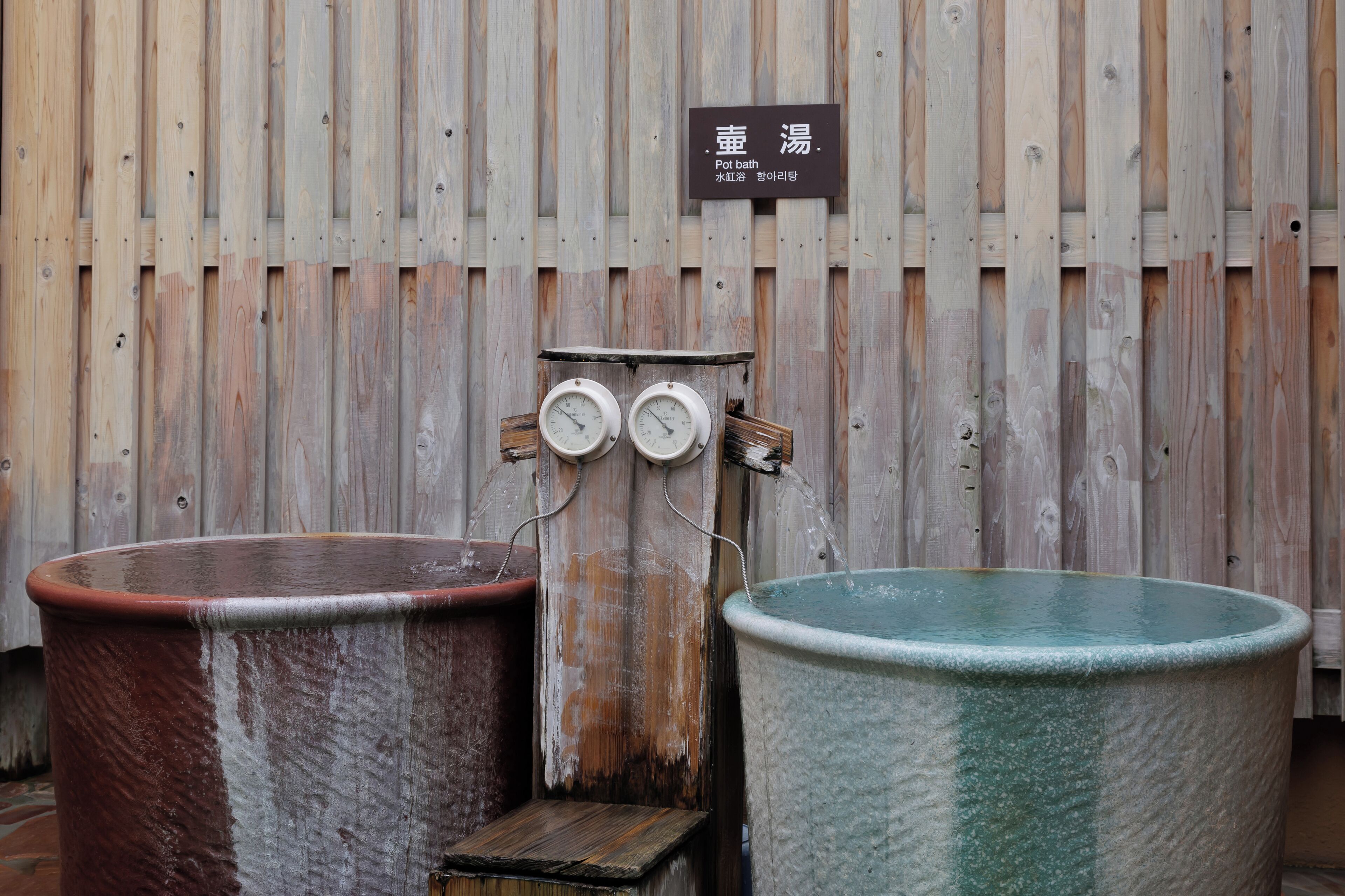 Two large stone tubs with a wooden wall and a sign above them.