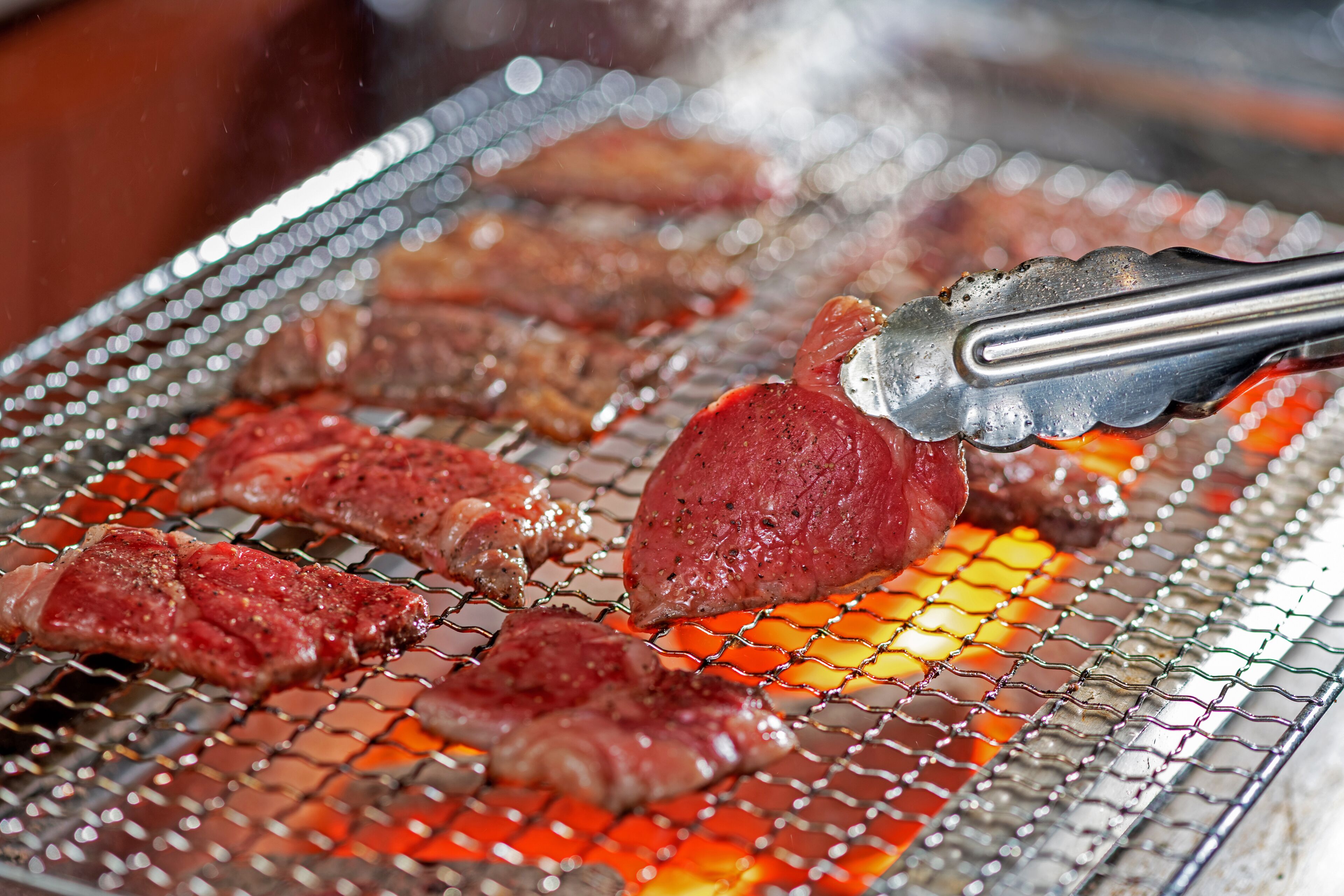 A close-up of meat grilling on a wire mesh over an open flame.