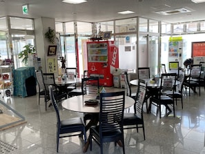 Un espacio interior limpio y moderno con mesas y sillas redondas, máquinas expendedoras y una vista despejada al exterior.