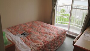 A hotel room with a bed, a desk, and a view of a body of water through a balcony. - Hotel Big Marine Amami (Amami)