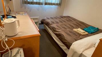 Une chambre d’hôtel avec un lit, un bureau doté d’une bouilloire, une chaise et une fenêtre avec des rideaux.