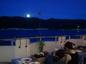 Una terraza con mesa lista para comer, con vistas a un cuerpo de agua y un paisaje montañoso.