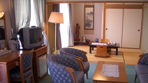 A hotel room with a TV, two blue patterned chairs, a wooden table, and a tatami mat floor. - Hotel Big Marine Amami (Amami)