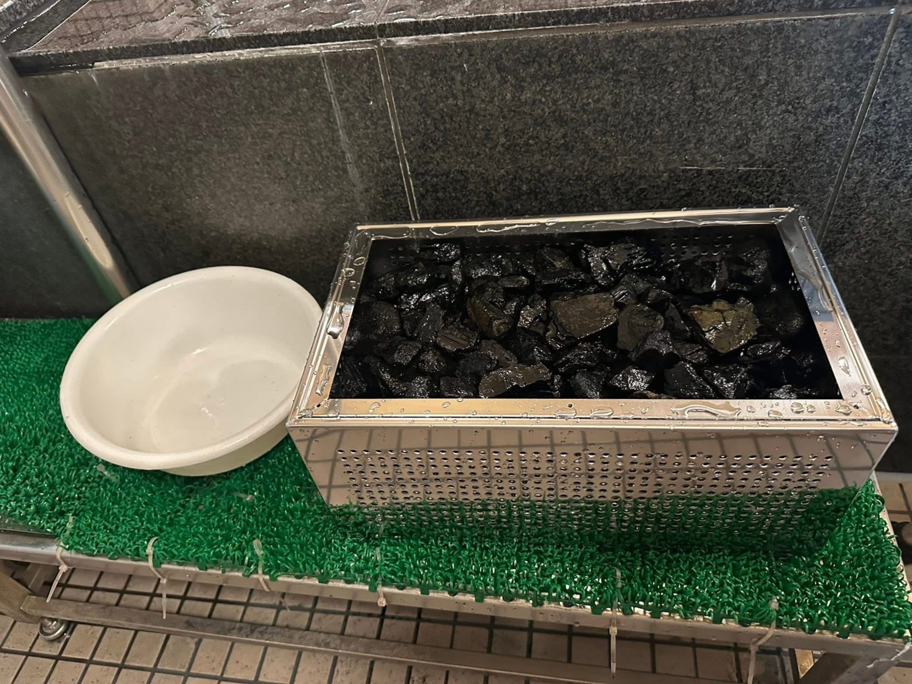 Een metalen bak met een rasterpatroon, op een groen oppervlak, naast een witte kom.