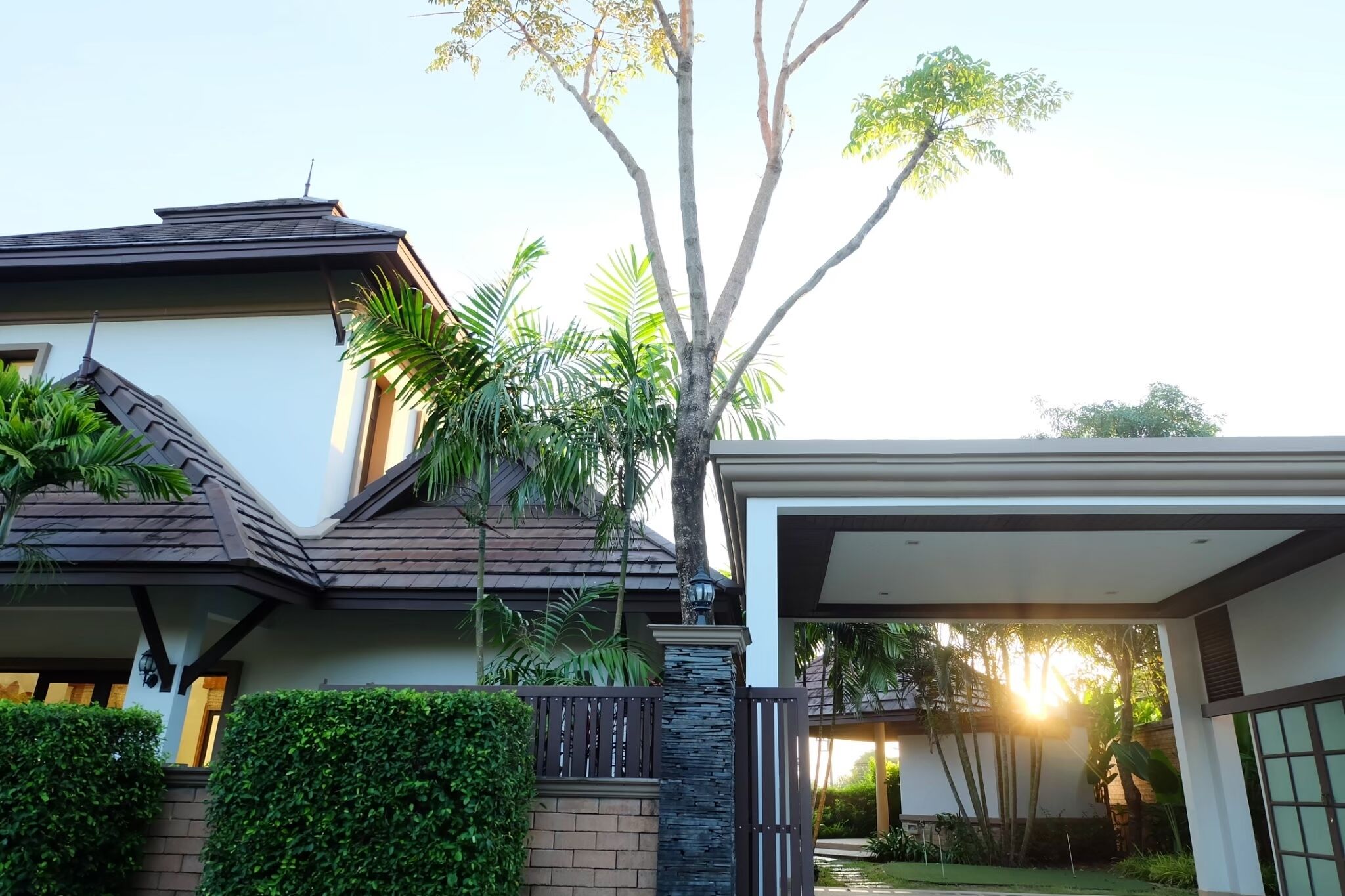 Una casa moderna con un porche cubierto, un muro de piedra y un árbol grande.
