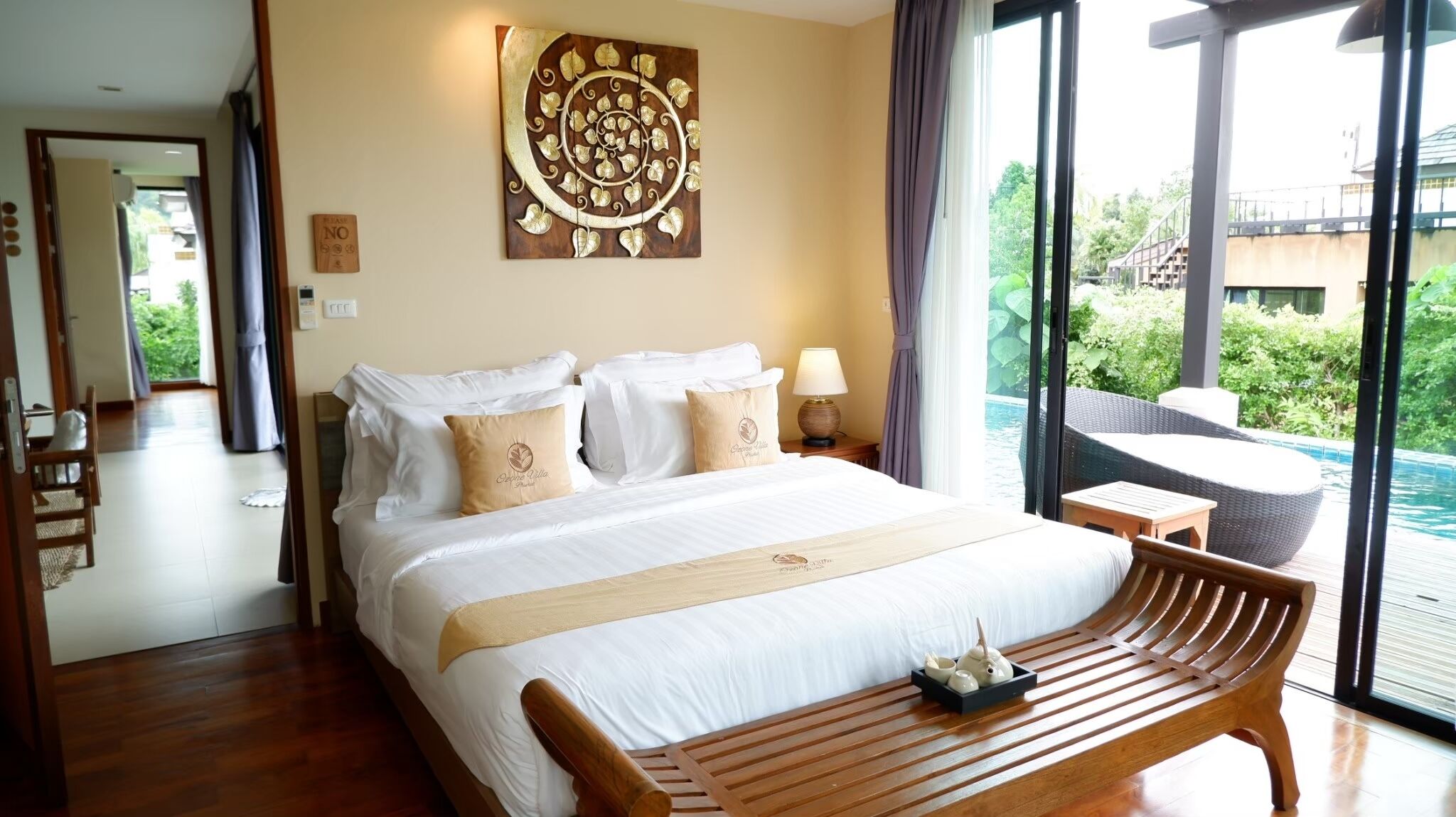 A hotel room with a large bed, a wooden bench, a view of a swimming pool, and a decorative wall piece.