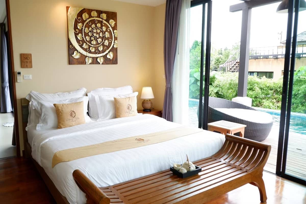 A hotel room with a large bed, a wooden bench, a view of a swimming pool, and a decorative wall piece.