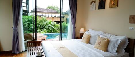 A hotel room with a bed, a bedside table, a lamp, and a view of a swimming pool.