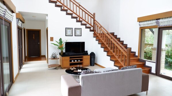 A living room with a staircase, a television, a sofa, and a window with a view. - Ozone Villa (Pa Klok)