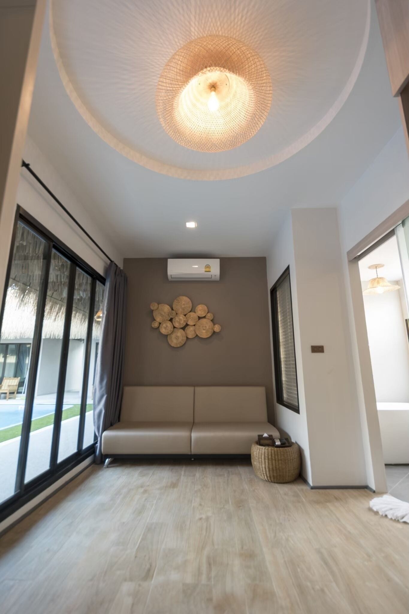 A modern interior with a ceiling light fixture, a wall-mounted air conditioner, a seating area, and a large window.