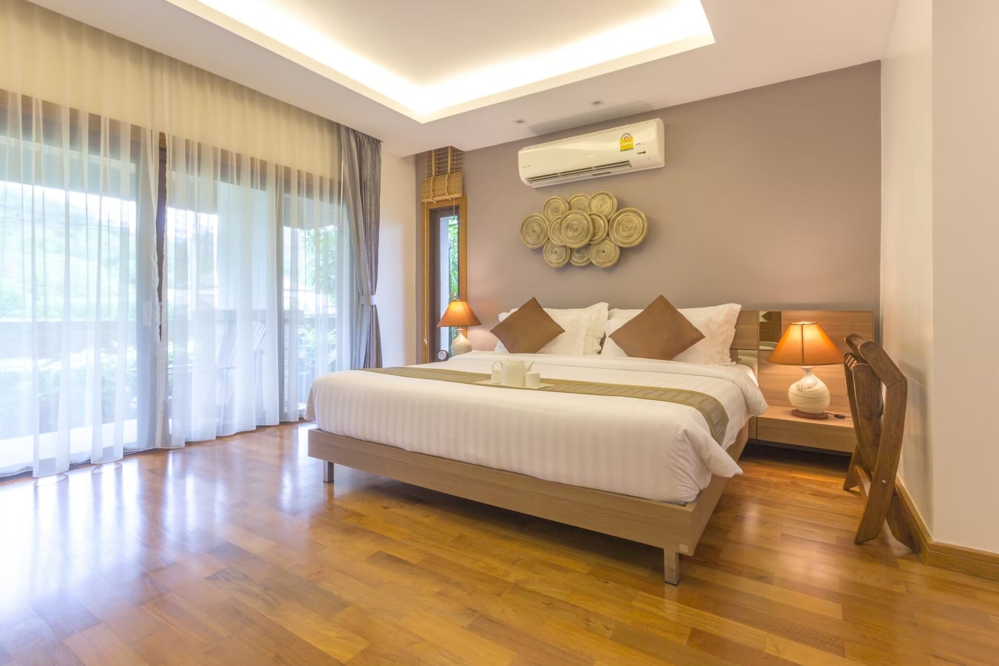 Une chambre d’hôtel moderne dotée d’un grand lit, d’un parquet, d’un luminaire au plafond, d’un climatiseur et offrant une vue sur la verdure environnante.