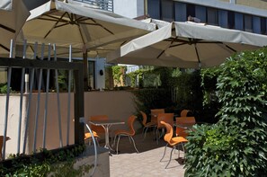 An outdoor patio area with tables and chairs, covered by large umbrellas, and surrounded by greenery. - Uliss Hotel (Odesa)