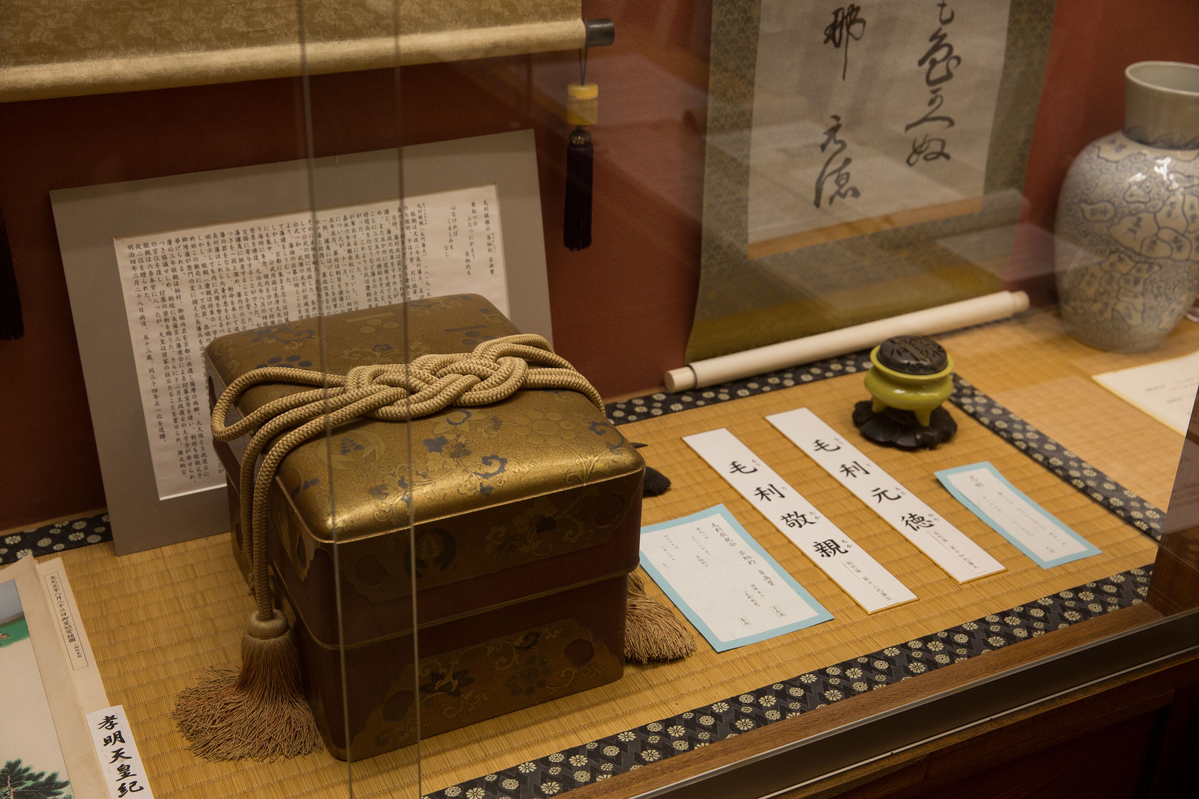 A display case with a traditional chest, a scroll, and a vase.