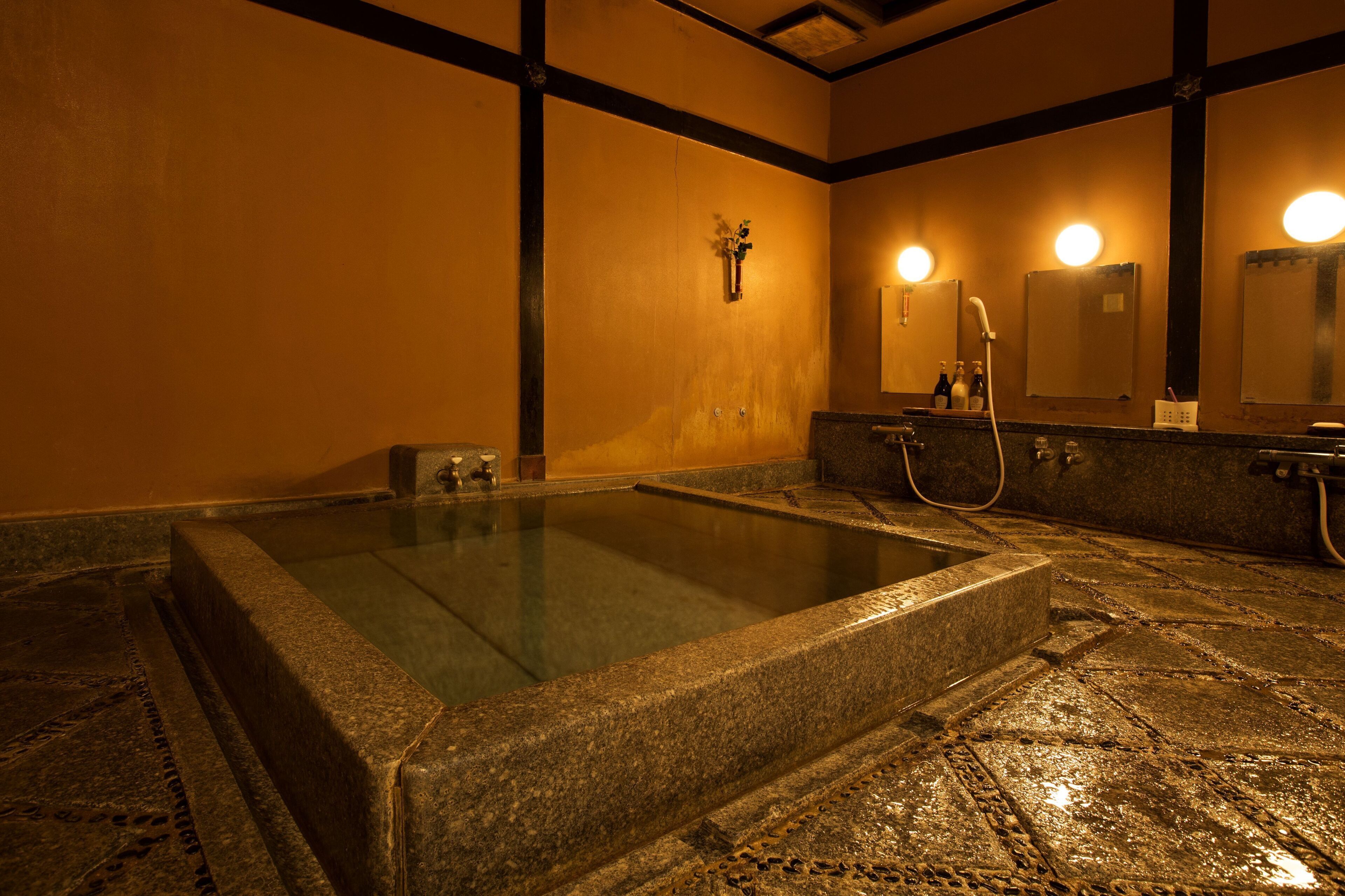 A stone hot tub in a room with a wooden ceiling and a large mirror.