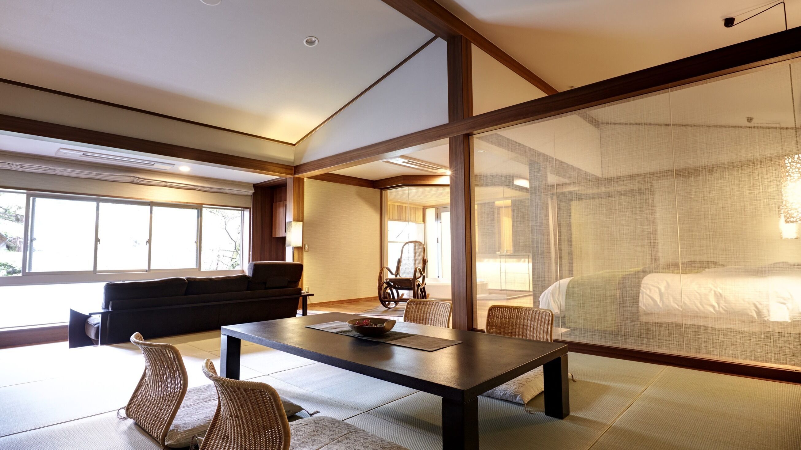 A modern hotel room with a large bed, a dining table, a sofa, and a chair.