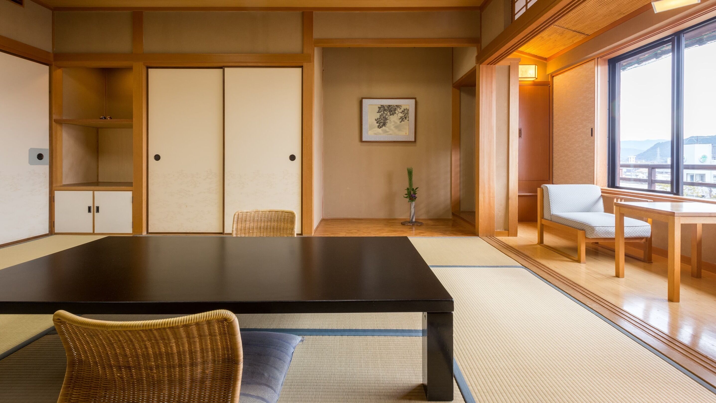 Ein traditioneller japanischer Raum mit Tatami-Bodenbelag, einem niedrigen Tisch, einem Stuhl und Schiebetüren.