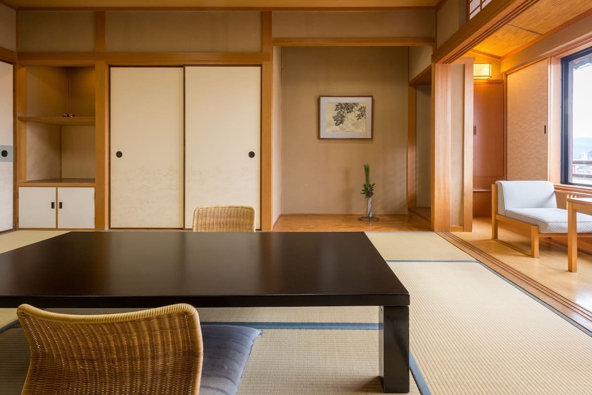 Una habitación tradicional japonesa con suelo de tatami, una mesa baja, una silla y puertas correderas.