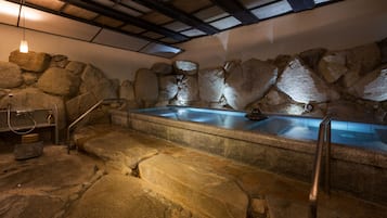 A stone-walled hot tub area with steps leading up to it, a metal handrail, and a stone basin.