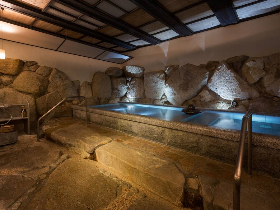 A stone-walled hot tub area with steps leading up to it, a metal handrail, and a stone basin.
