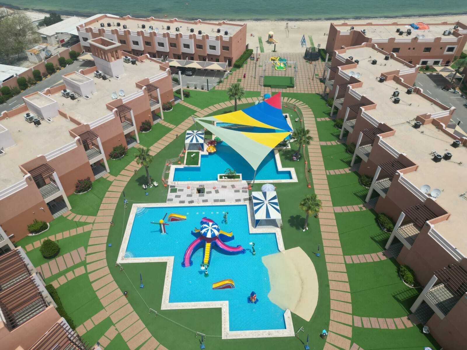 A resort with a central swimming pool, multiple balconies, and a beach area.