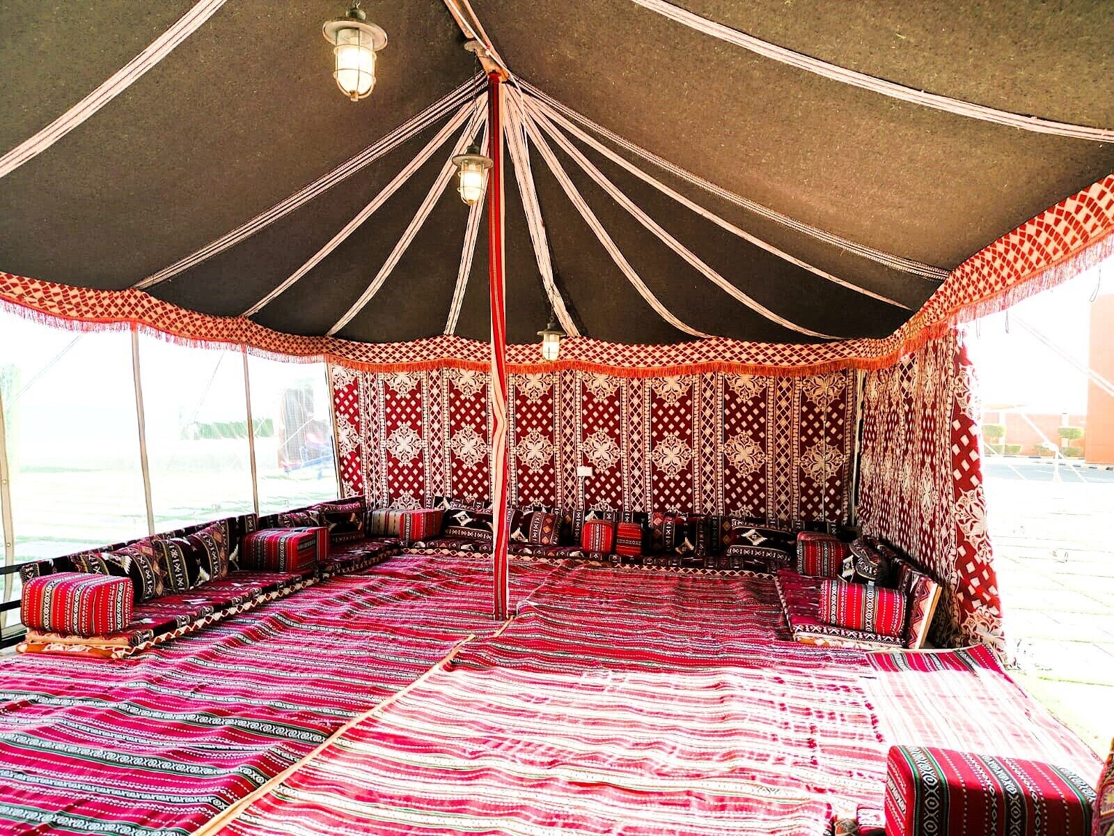 A tent with a patterned interior, multiple seating areas, and hanging lights.