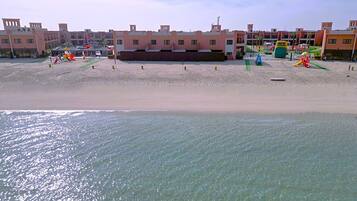 A beach with clear water, a sandy shore, and buildings in the background.