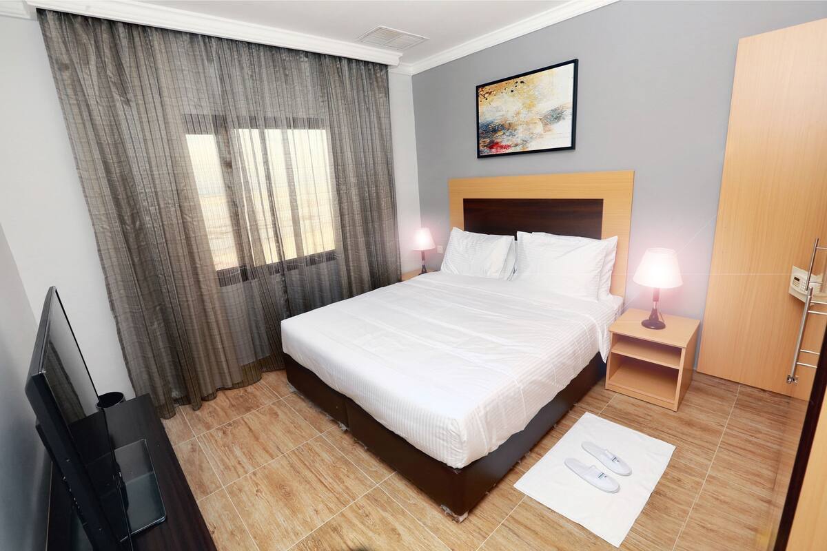 Ein Hotelzimmer mit einem großen Bett, zwei Nachttischlampen, einem Fernseher und einem Gemälde an der Wand.