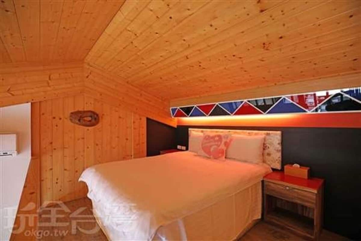 Una habitación con paneles de madera, una cama, una mesita de noche y un estante fijado a la pared.