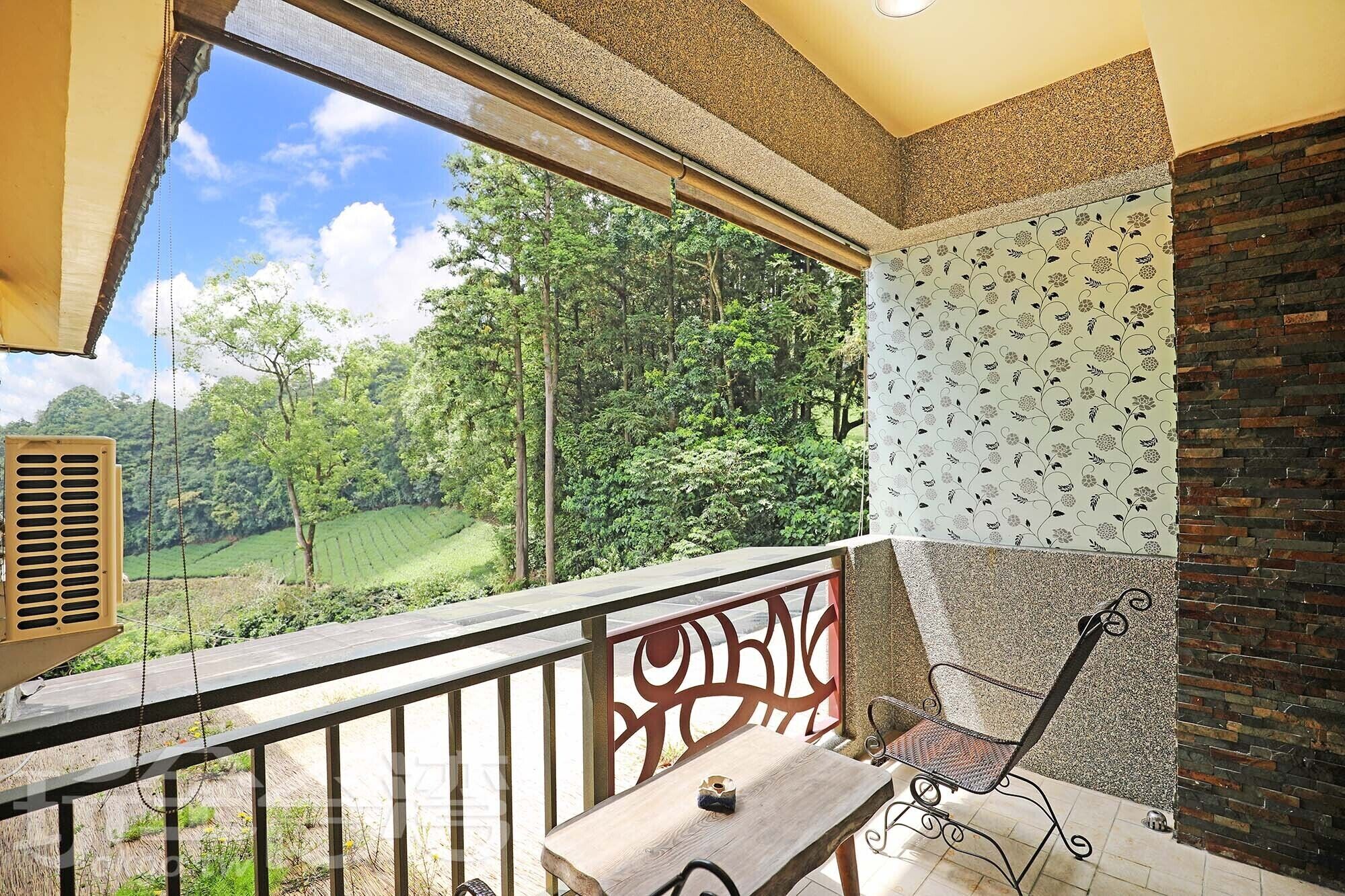 A balcony with a view of a green landscape, a patterned wall, and a metal chair.