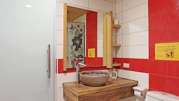 A bathroom with a wooden ceiling, white tiled walls, a red accent wall, a wooden vanity with a bowl sink, a mirror, and a toilet with floral designs.