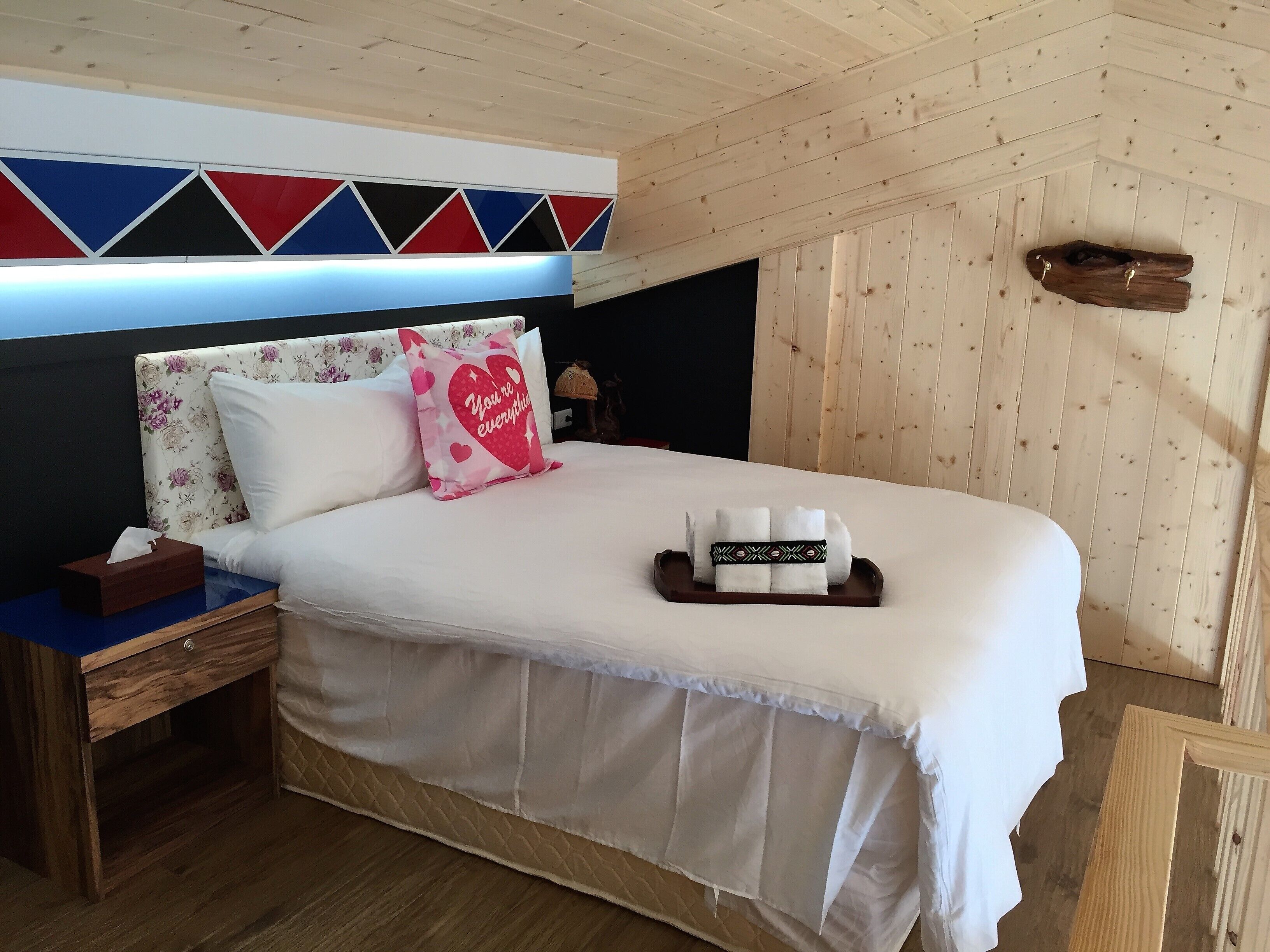 A neatly made bed with a floral headboard, a bedside table with a tissue box, and a decorative pillow.